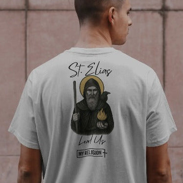 Person wearing a t-shirt with 'St. Elias' design on the back against a tiled wall.